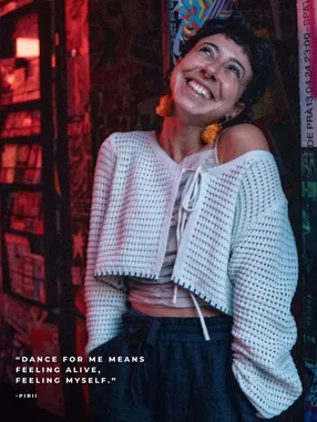Portrait of an XD community member smiling in red light and wearing a white knit top, with a personal quote
